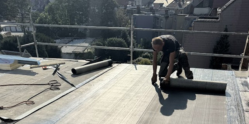 Un couvreur applique un rouleau de membrane bitumineuse chauff&eacute;e pour assurer l&rsquo;&eacute;tanch&eacute;it&eacute; d&rsquo;une toiture plate.