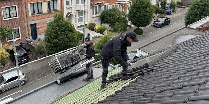 deux ouvriers sont sur une toiture en tuile noire, l'un pose des tuiles sur le toit et l'autre prépare du matériel