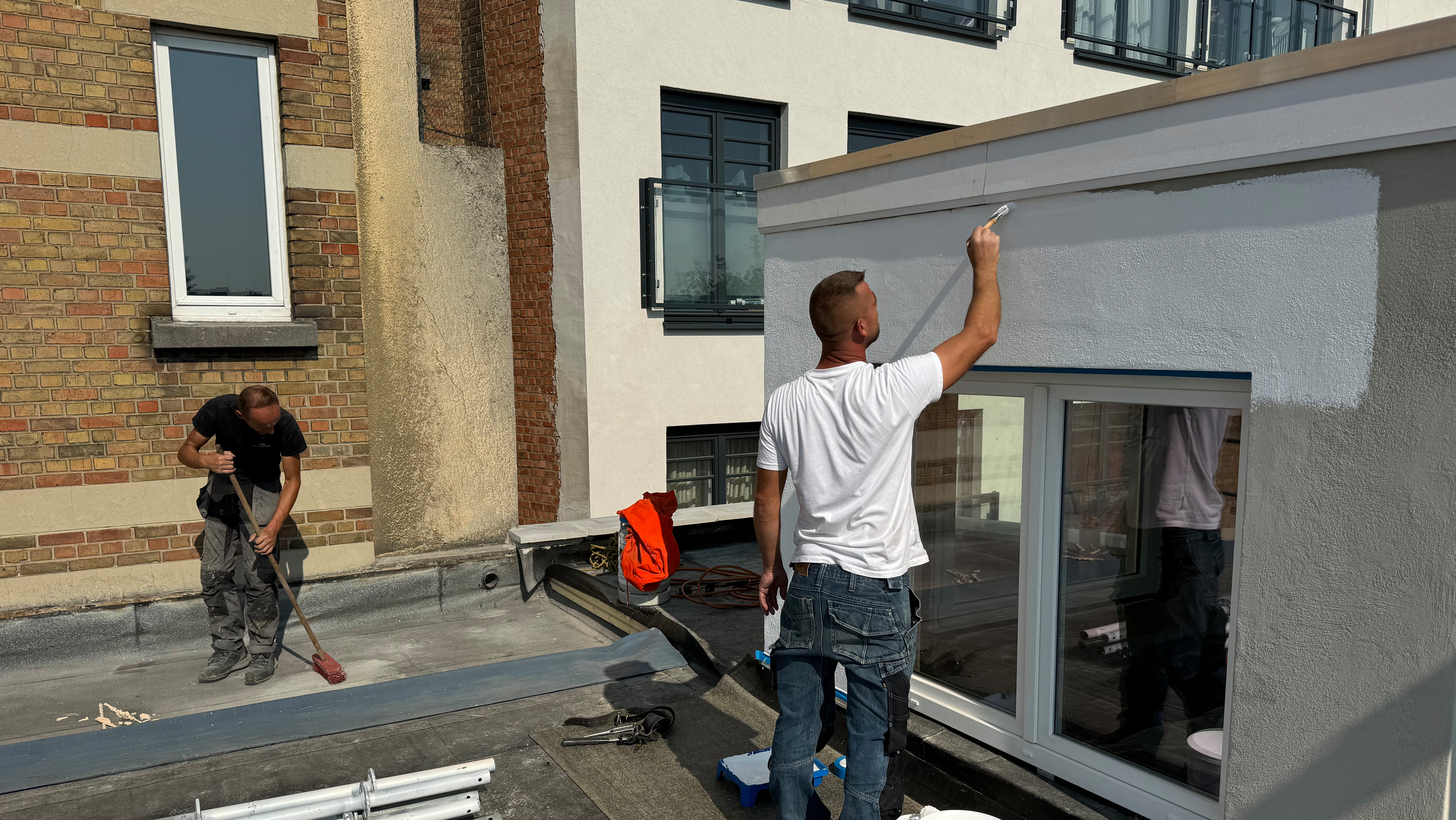 un ouvrier peint la façade en blanc pendant qu'un autre nettoie le chantier